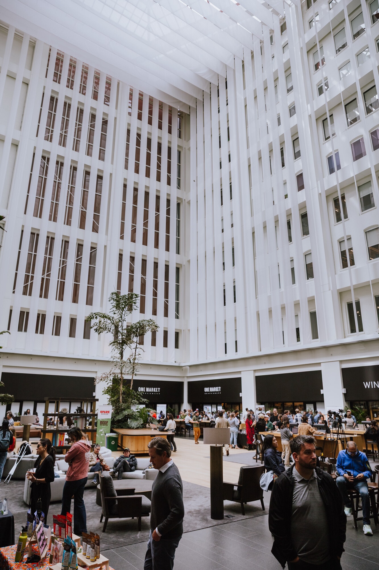 The One Market Plaza atrium, looking up past the white fins to the skylight, with tenants in the lobby below