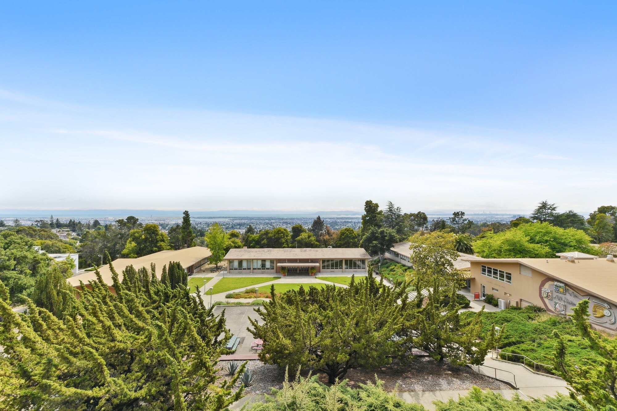 The Oakland Campus seen from the hillside: low campus buildings among the trees, with the bay beyond